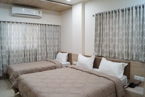 Ein Hotelzimmer mit zwei Betten, beiger Bettwäsche, einer Klimaanlage und gemusterten Vorhängen.