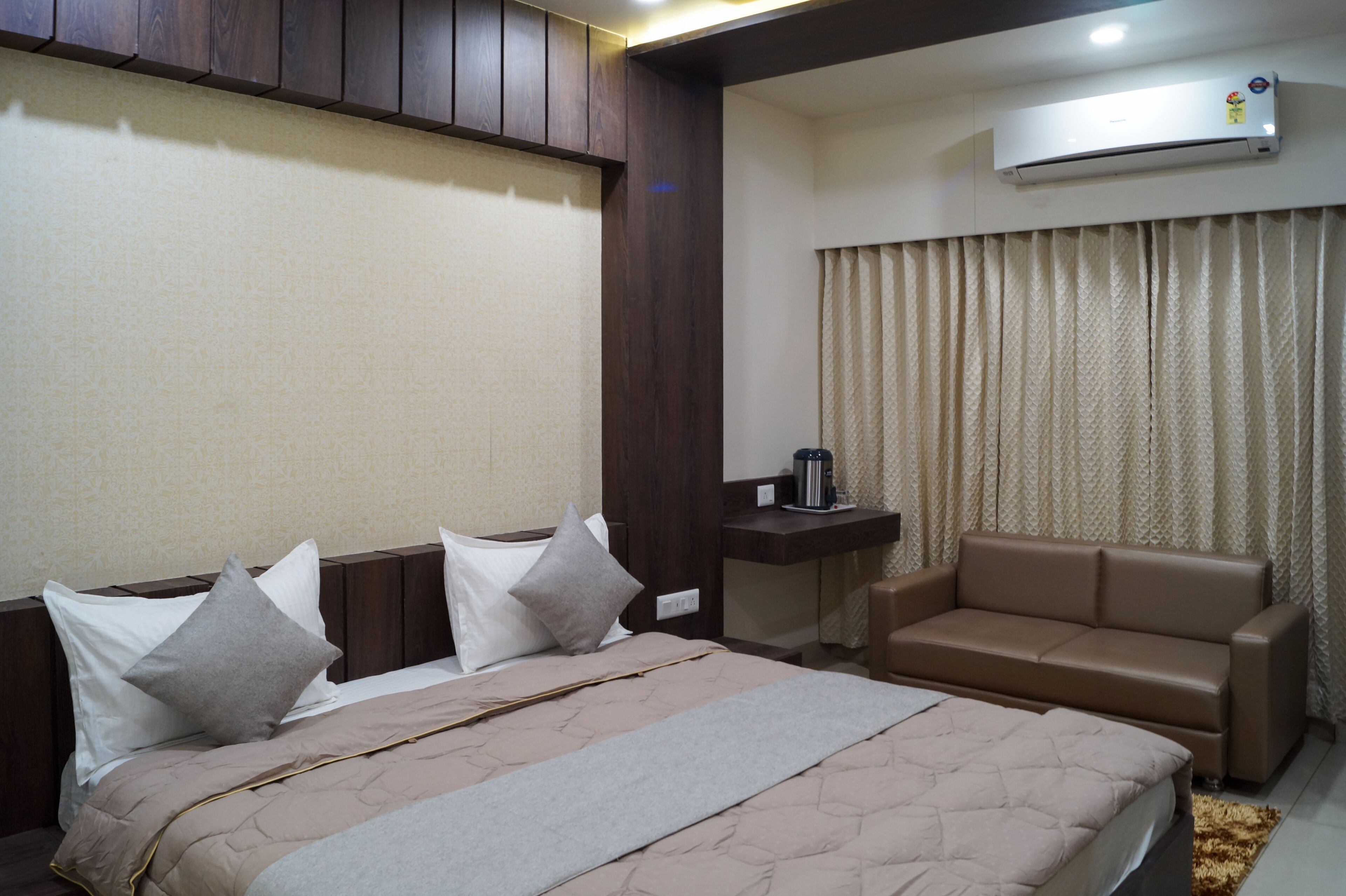 A hotel room with a bed, a sofa, an air conditioning unit, and a curtain.
