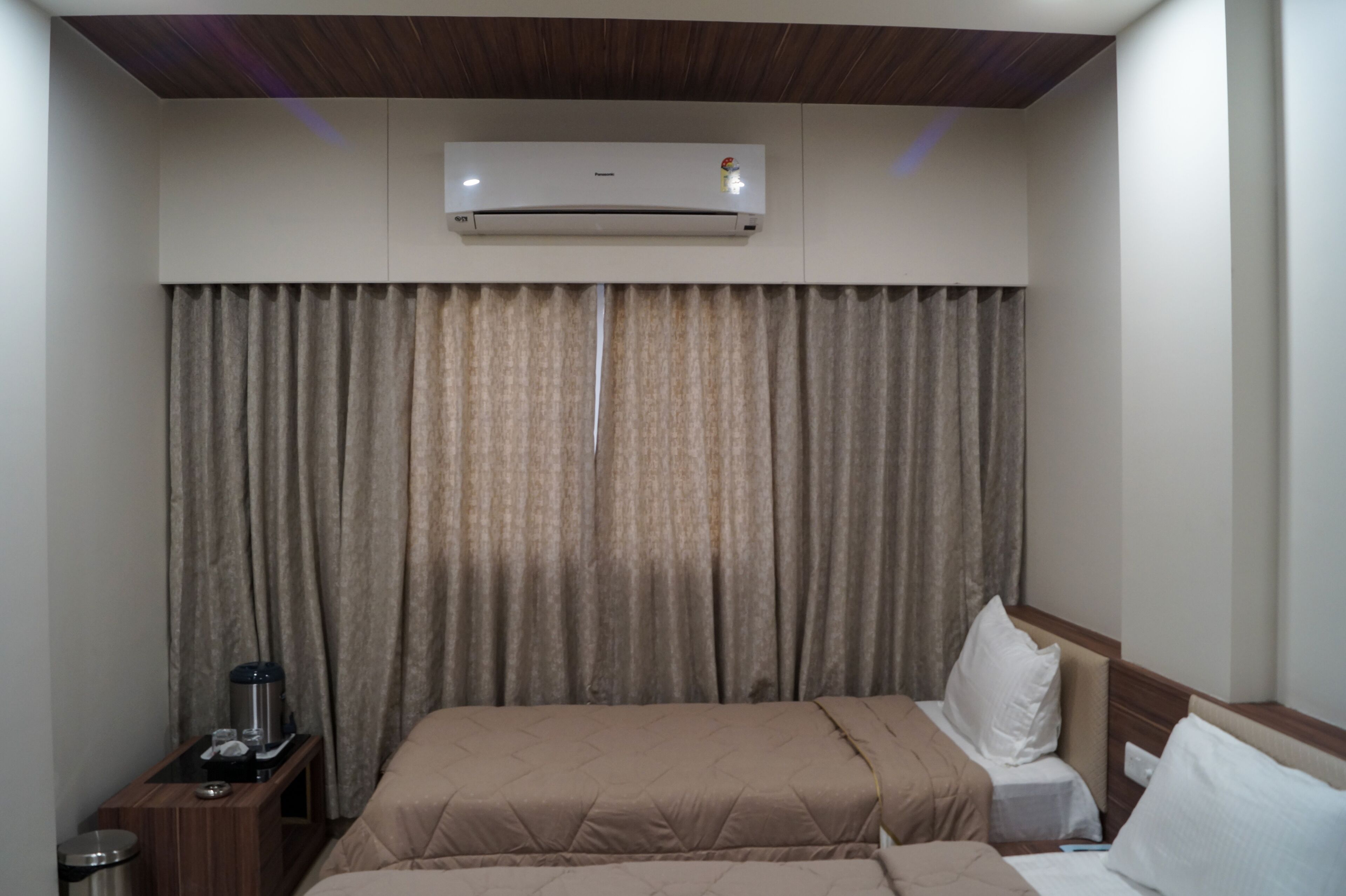 A hotel room with a bed, a nightstand, an air conditioning unit, and a curtain.