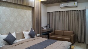 A hotel room with a bed, a desk, a chair, and an air conditioning unit.