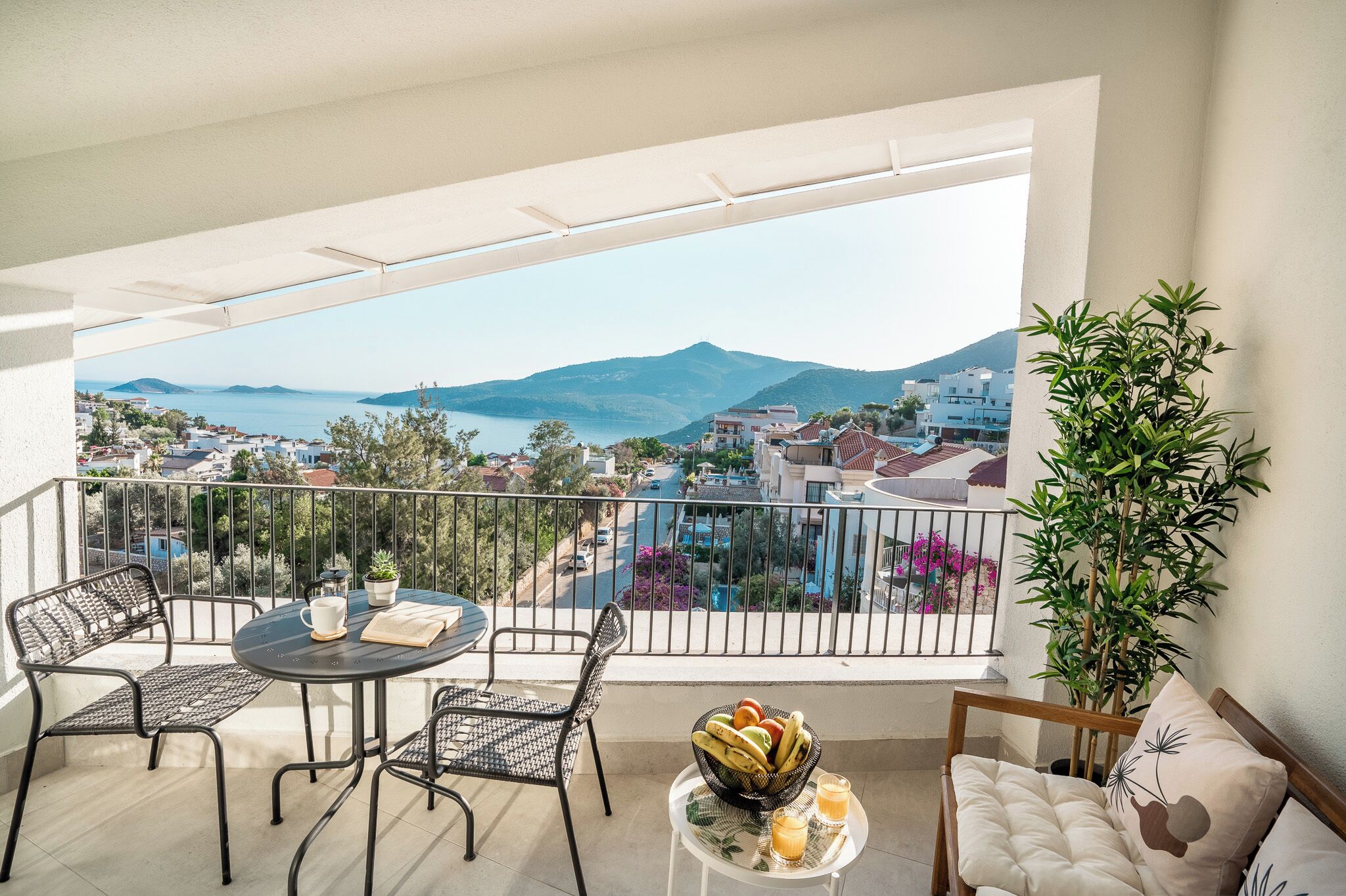 A balcony with a table, chairs, a bowl of fruit, and a potted plant.