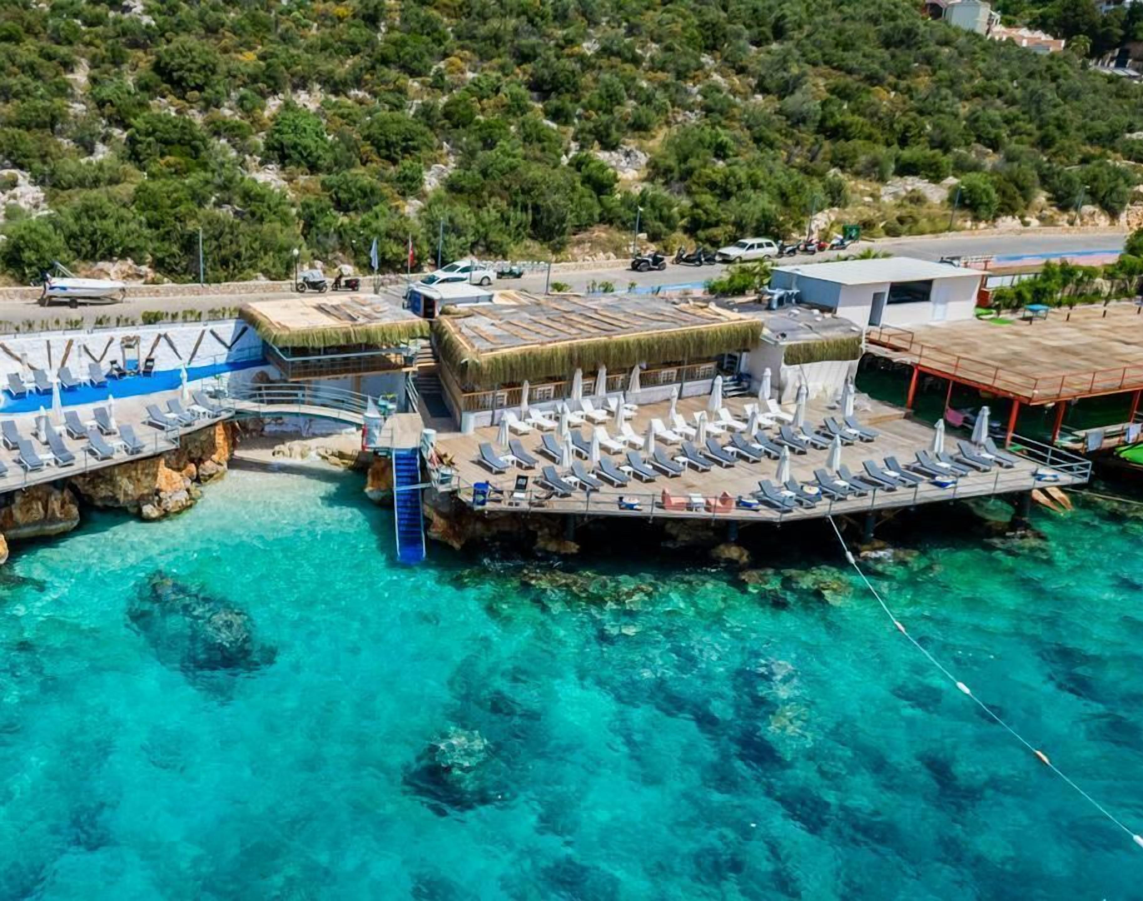 Vista aérea de un resort con un muelle, agua turquesa cristalina y montañas al fondo.