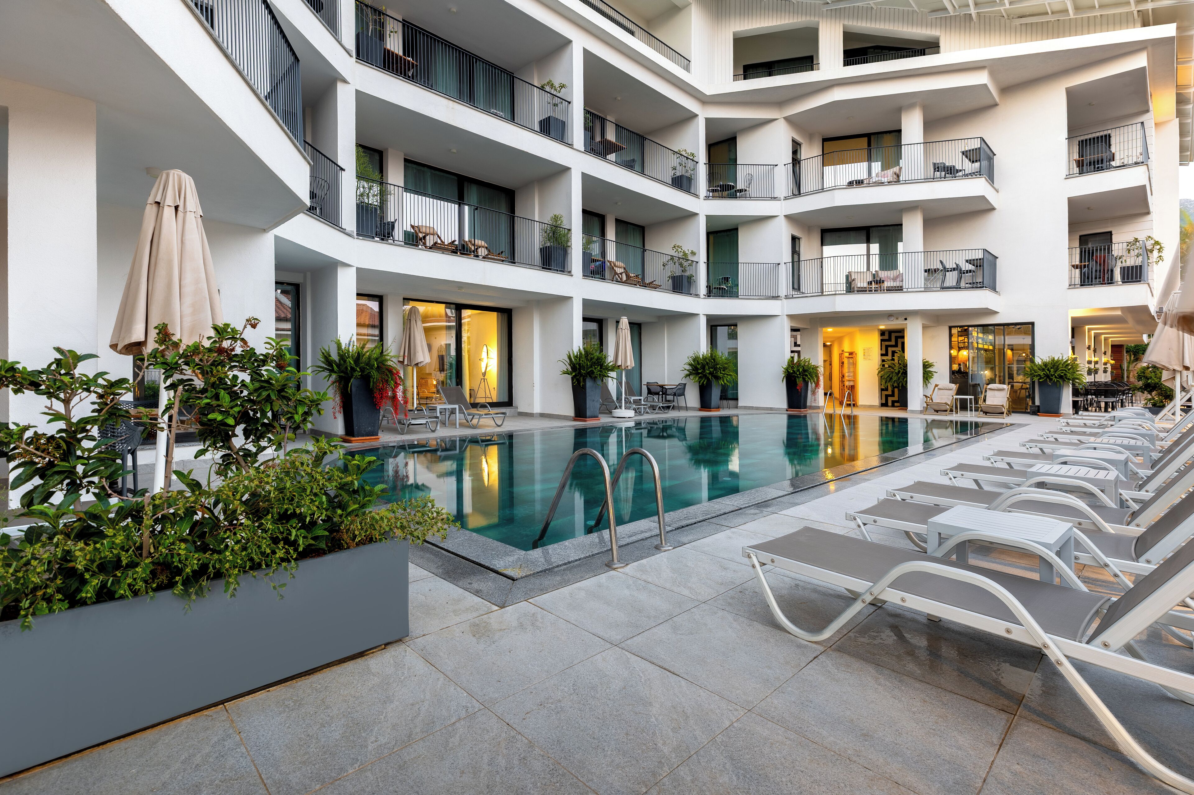 A multi-level indoor pool area with lounge chairs and potted plants.