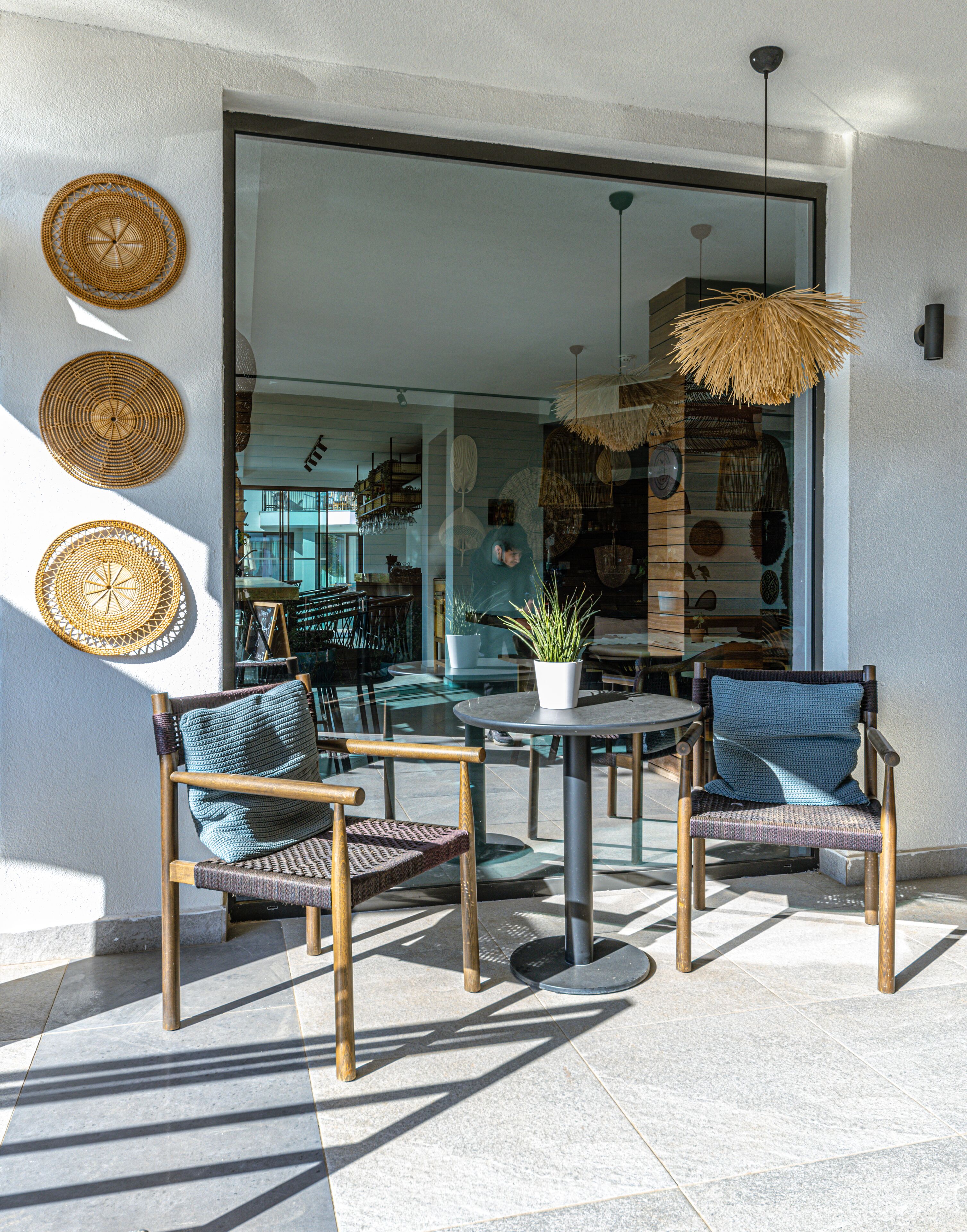 Un espace extérieur aménagé avec deux fauteuils en osier, une table ronde et un luminaire suspendu.