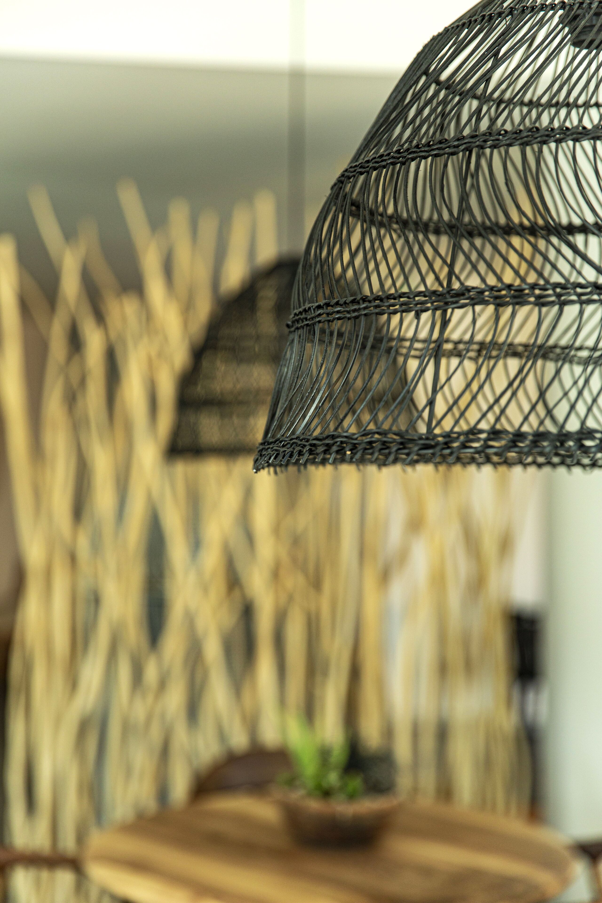 Gros plan d’un luminaire en métal tressé, avec un arrière-plan flou composé de structures verticales évoquant du bambou.