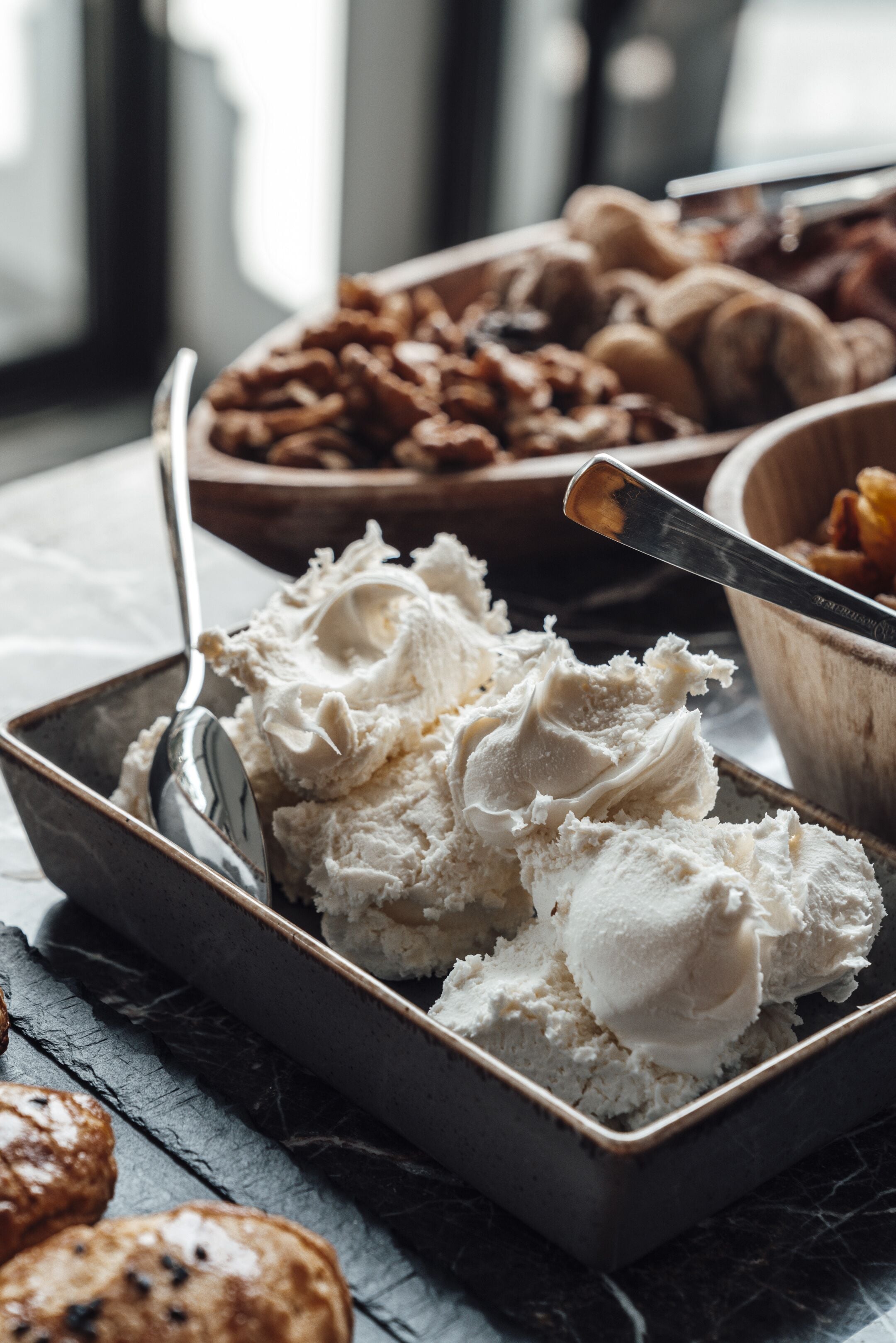 A tray of ice cream with a spoon, a bowl of cookies, and a bowl of nuts on a table.