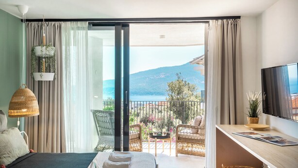 A hotel room with a bed, a desk, a TV, and a balcony with a view of the sea. - Payava Hotel by True Blue (Kas)