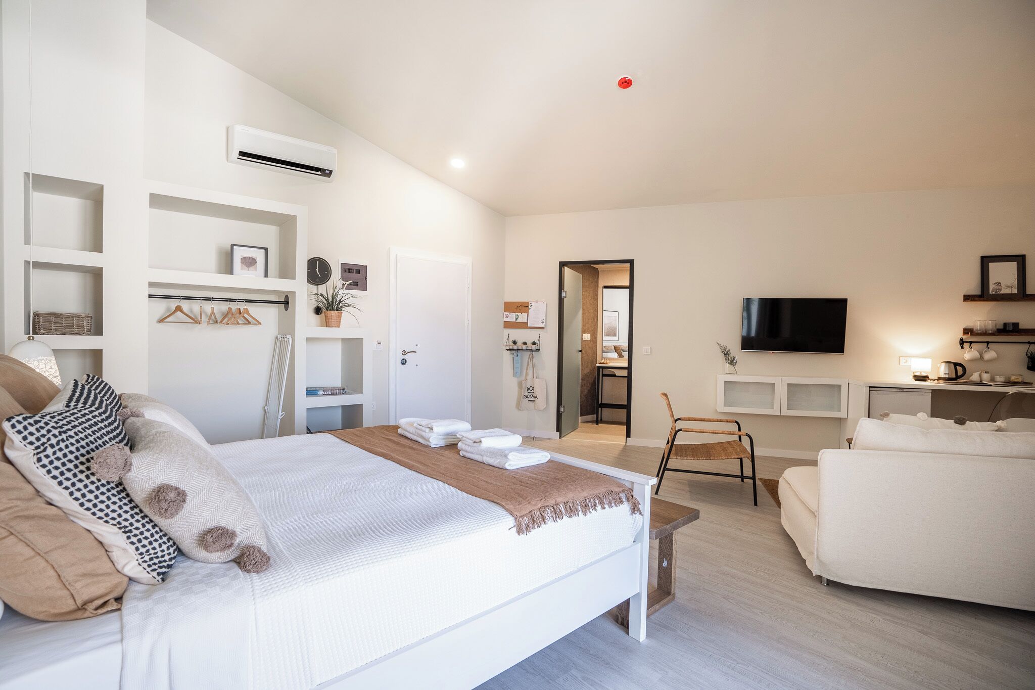 Une chambre moderne comprenant un lit, des tables de chevet, un téléviseur et un coin salon avec un canapé et un fauteuil.