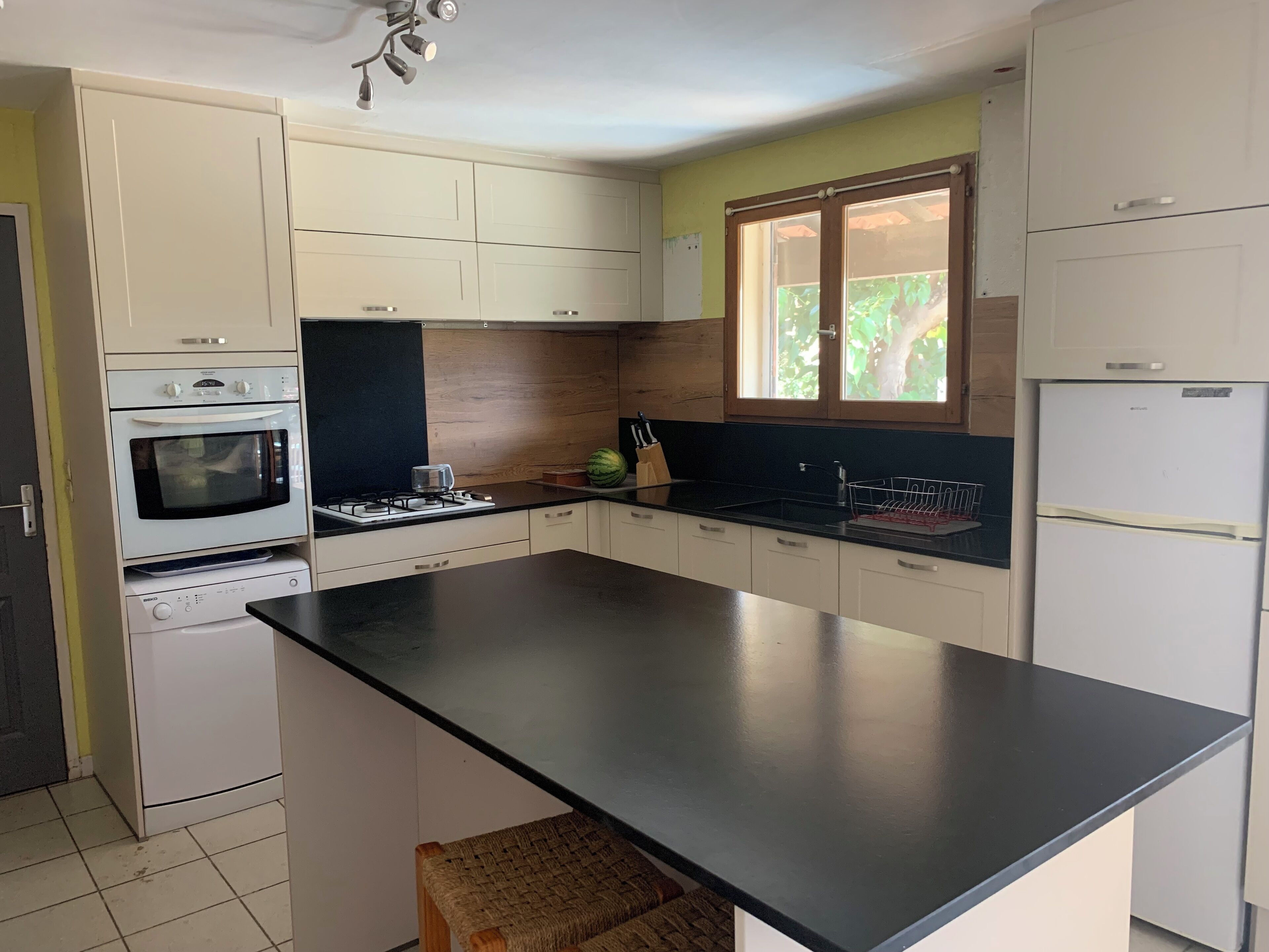 A kitchen with a central island, white cabinets, a built-in oven, a refrigerator, and a window with a view of greenery.