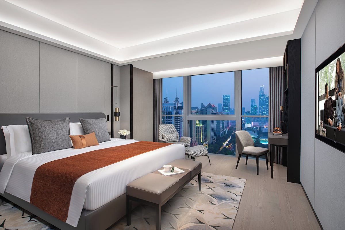Habitación de hotel moderna con una cama grande, un escritorio y vistas a la silueta urbana.