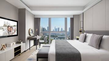 A modern hotel room with a large bed, a desk, a TV, and a city view.