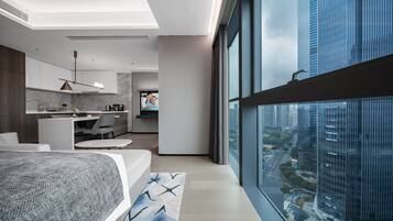A modern bedroom with a large bed, a view of the city through floor-to-ceiling windows, a kitchen area, and a living space with a sofa and coffee table.