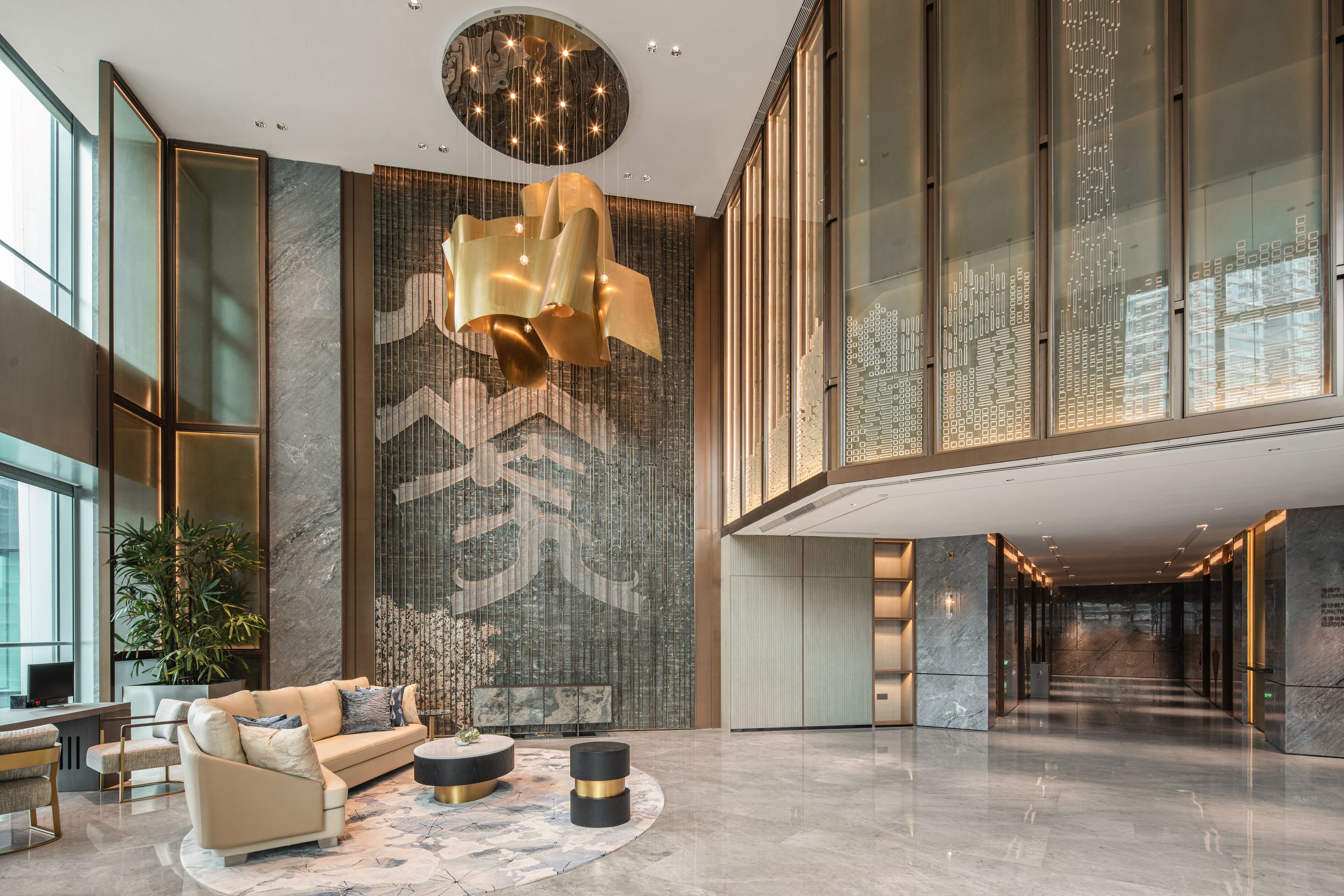 Eine großzügige Lobby mit einem modernen Kronleuchter, einer Sitzecke mit Sofa und Couchtisch sowie einer großen Wand mit vertikalen Mustern.