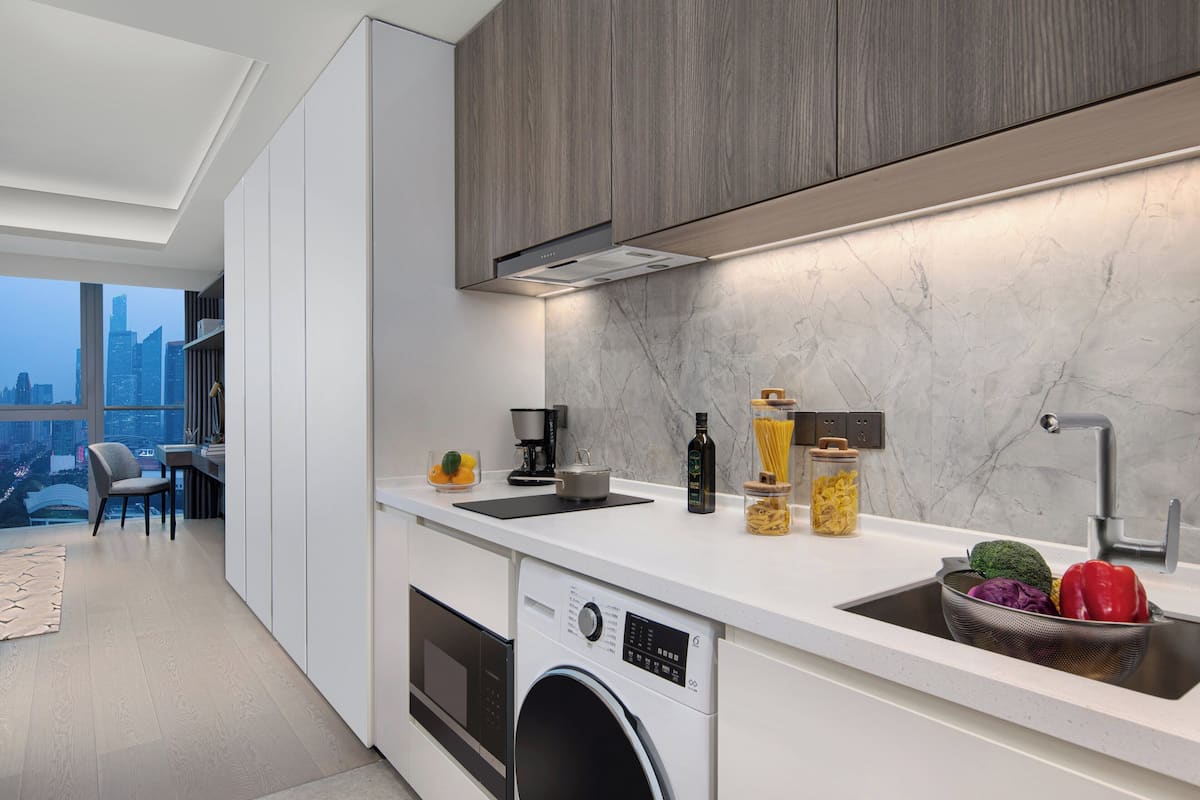 Una cocina moderna con lavadora integrada, un lavabo con colador y vistas a la ciudad a través de amplios ventanales.