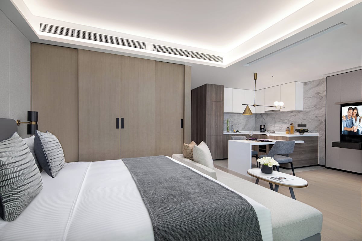 Una habitación de hotel moderna con una cama grande, un pequeño rincón de estar, una zona de cocina y un televisor.