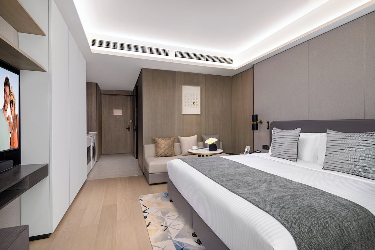 Una habitación de hotel moderna con una cama grande, televisión, sofá y una mesita.