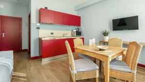 A compact living space with a kitchenette, a dining area with wicker chairs, and a flat-screen TV mounted on the wall.