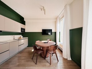 Een kleine keuken met een eethoek, een flatscreen tv aan de muur en een raam met gordijnen.