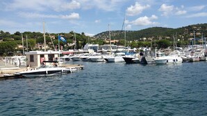 Una marina con barcos amarrados, un pequeño edificio y un paisaje montañoso al fondo.