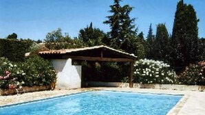 Una piscina con un pequeño pabellón, rodeada de abundante vegetación y árboles altos.