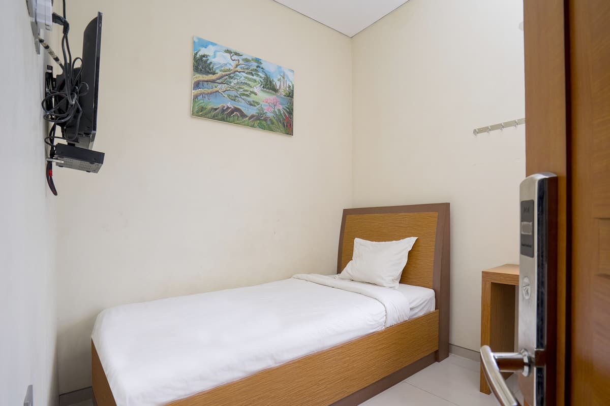A single bed with a wooden headboard, a painting on the wall, and a door with a handle.