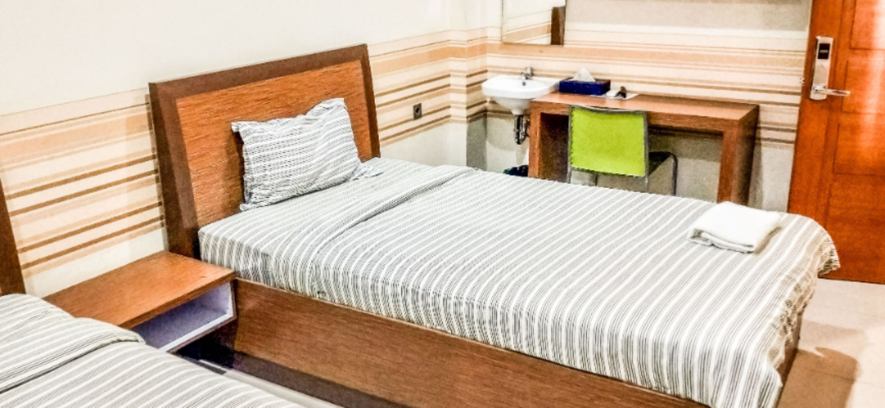 A hotel room with a bed, a nightstand, a mirror, and a sink.
