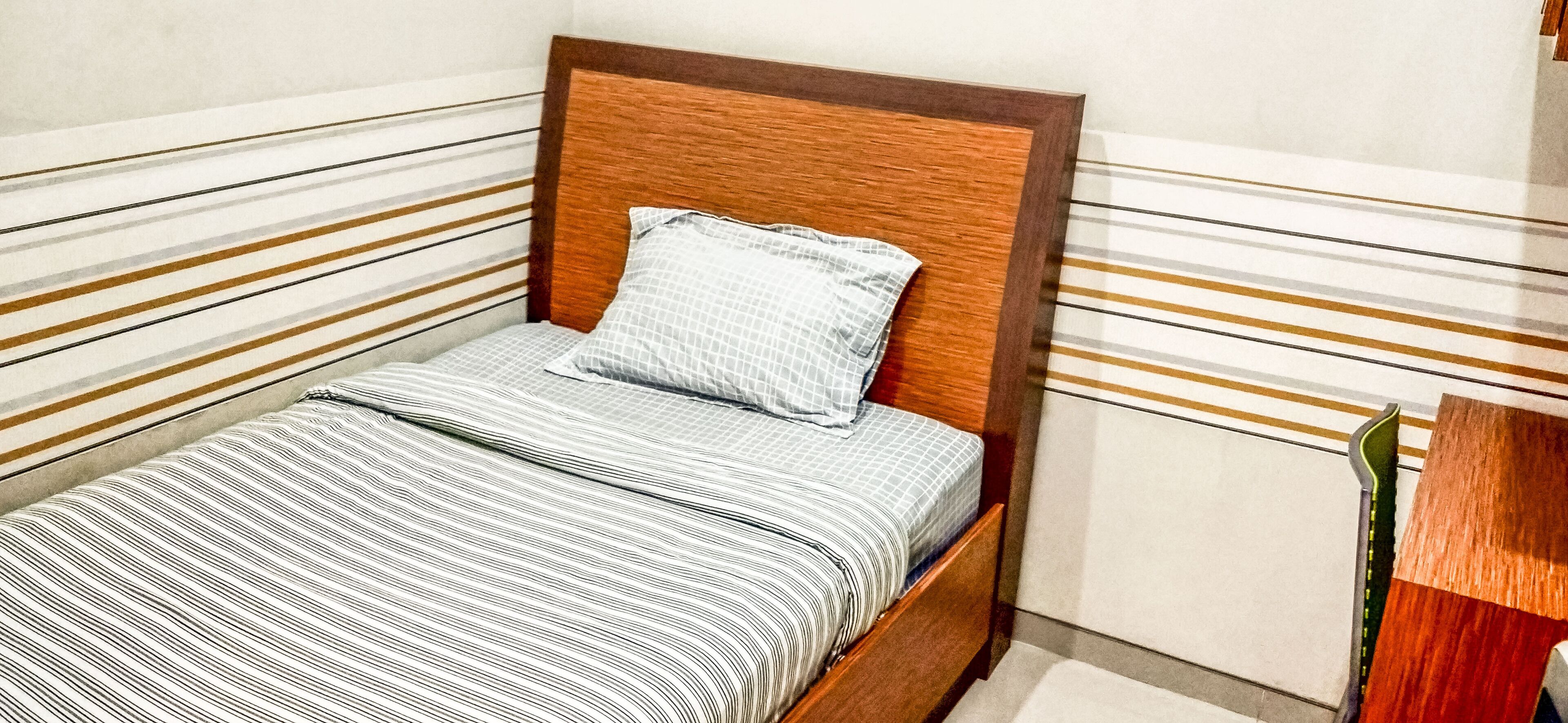A single bed with a wooden headboard, a striped bedspread, and a single pillow.