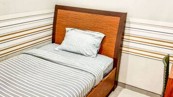 Un lit simple avec une tête de lit en bois, une couvre-lit à rayures et un seul oreiller.