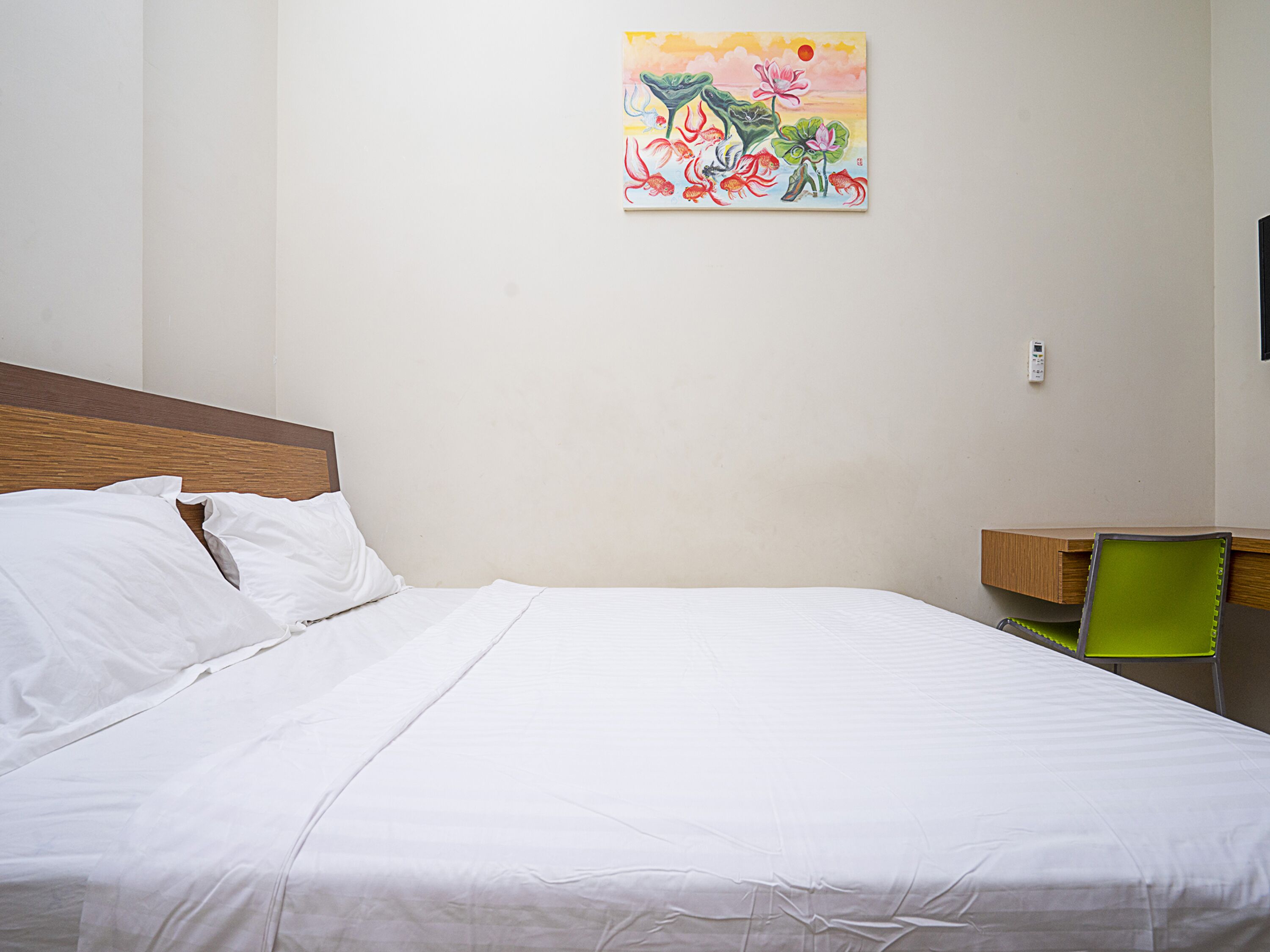 Una cama bien tendida con sábanas blancas, cabecera de madera y un cuadro colorido en la pared.