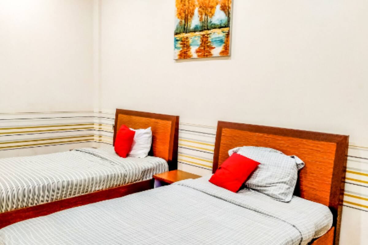 A hotel room with two single beds, striped bedding, wooden headboards, and a painting on the wall.