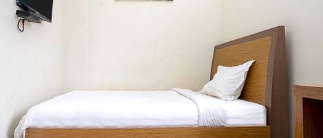A single bed with a wooden headboard and white bedding in a room with a plain wall and a painting.