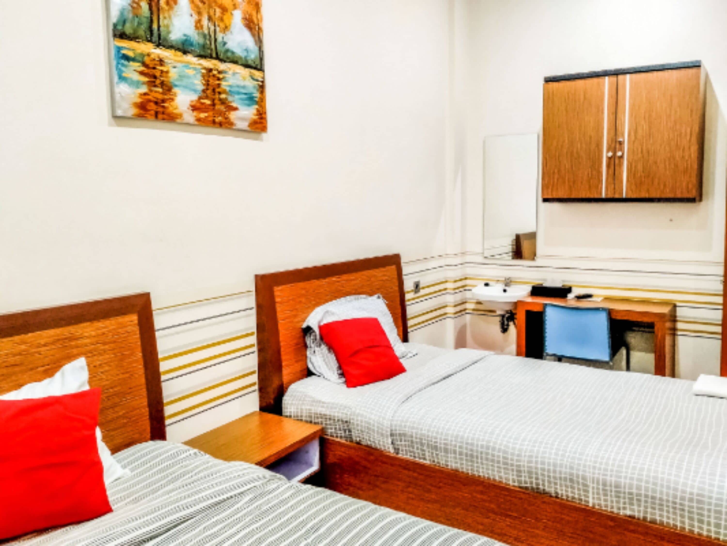 A hotel room with two beds, a wooden headboard, a bedside table, a mirror, a sink, and a cabinet.
