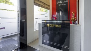Ein Empfangsschalter mit Glastrennwand, eine rote Akzentwand und ein Schild mit der Aufschrift 'Pandak Indah Rumah Kost'.