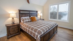 Una camera da letto con un letto di legno, due comodini con lampade, un'ampia finestra vista panoramica e un soffitto spiovente.
