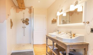 Ein Badezimmer mit Dusche, zwei Waschbecken, einem Holz-Waschtisch und einem großen Spiegel.