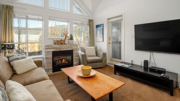 A living room with a fireplace, a sofa, a coffee table, a TV, and large windows.
