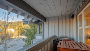 A balcony with a wooden table and grill, overlooking a paved area with trees and a distant building.
