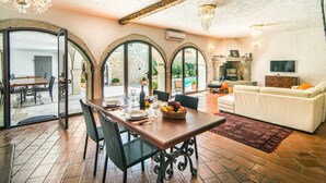 A dining area with a wooden table and chairs, a TV in the living room, and a stone wall. - Villa Marko (Vrsar)