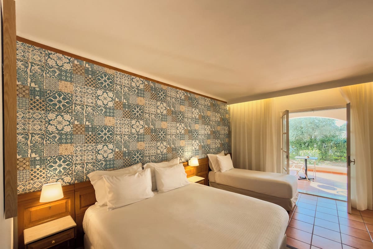 Een hotelkamer met twee bedden, een behang met patroon en uitzicht op het omliggende landschap.