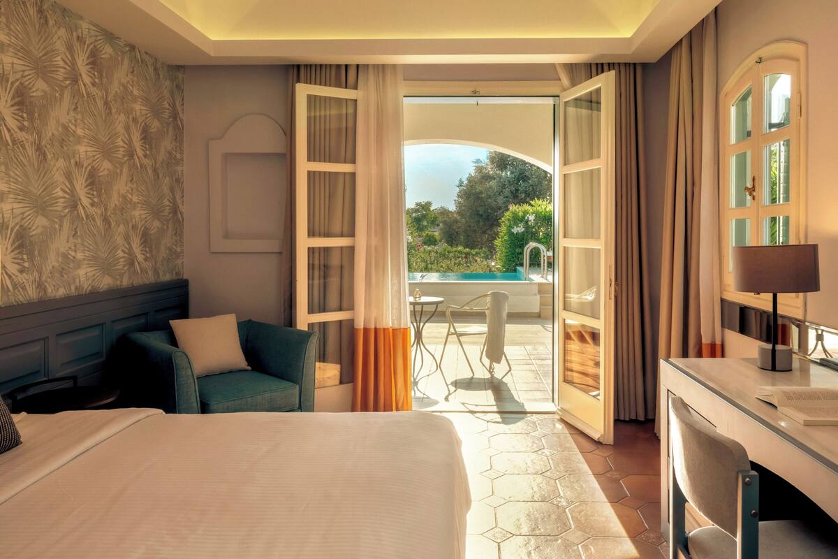 Een hotelkamer met een bed, een bureau en een open deur naar een zwembad.