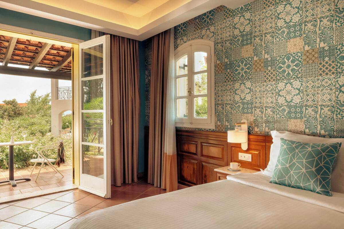 Een slaapkamer met een bed, nachtkastje, raam en uitzicht op de omgeving.