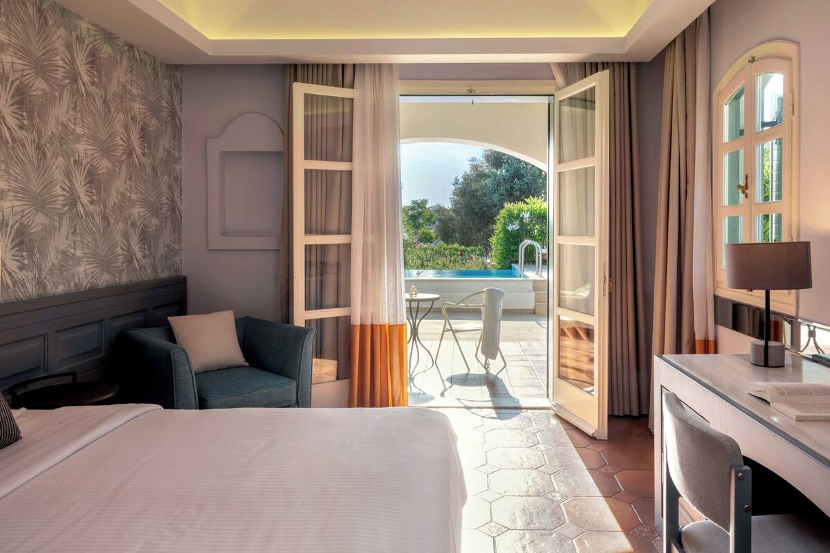 Een hotelkamer met een bed, een bureau en uitzicht op een buitenzwembad.