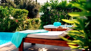A wooden deck with two lounge chairs, a small table, and a pool in the background. - Zeus Eretria Resort  (Eretria)
