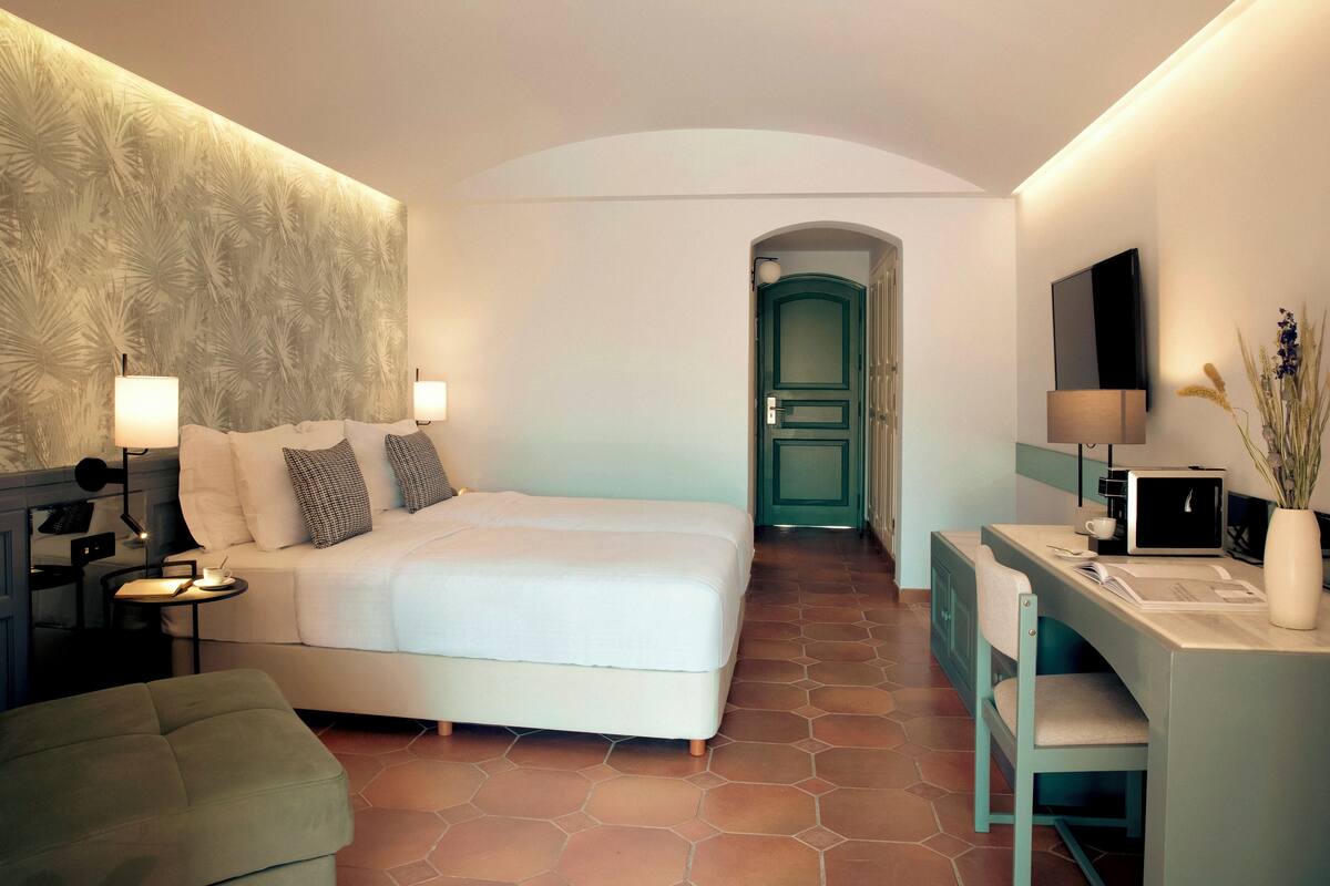 Een moderne hotelkamer met een groot bed, een bureau met een computer, een stoel en een televisie aan de muur.