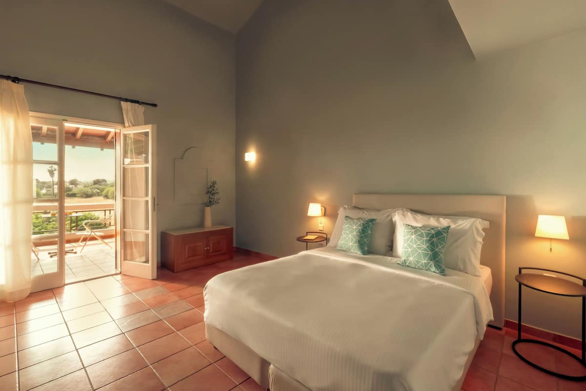 Een slaapkamer met een groot bed, twee bedlampen, een nachtkastje en een schuifdeur naar een buitenruimte.