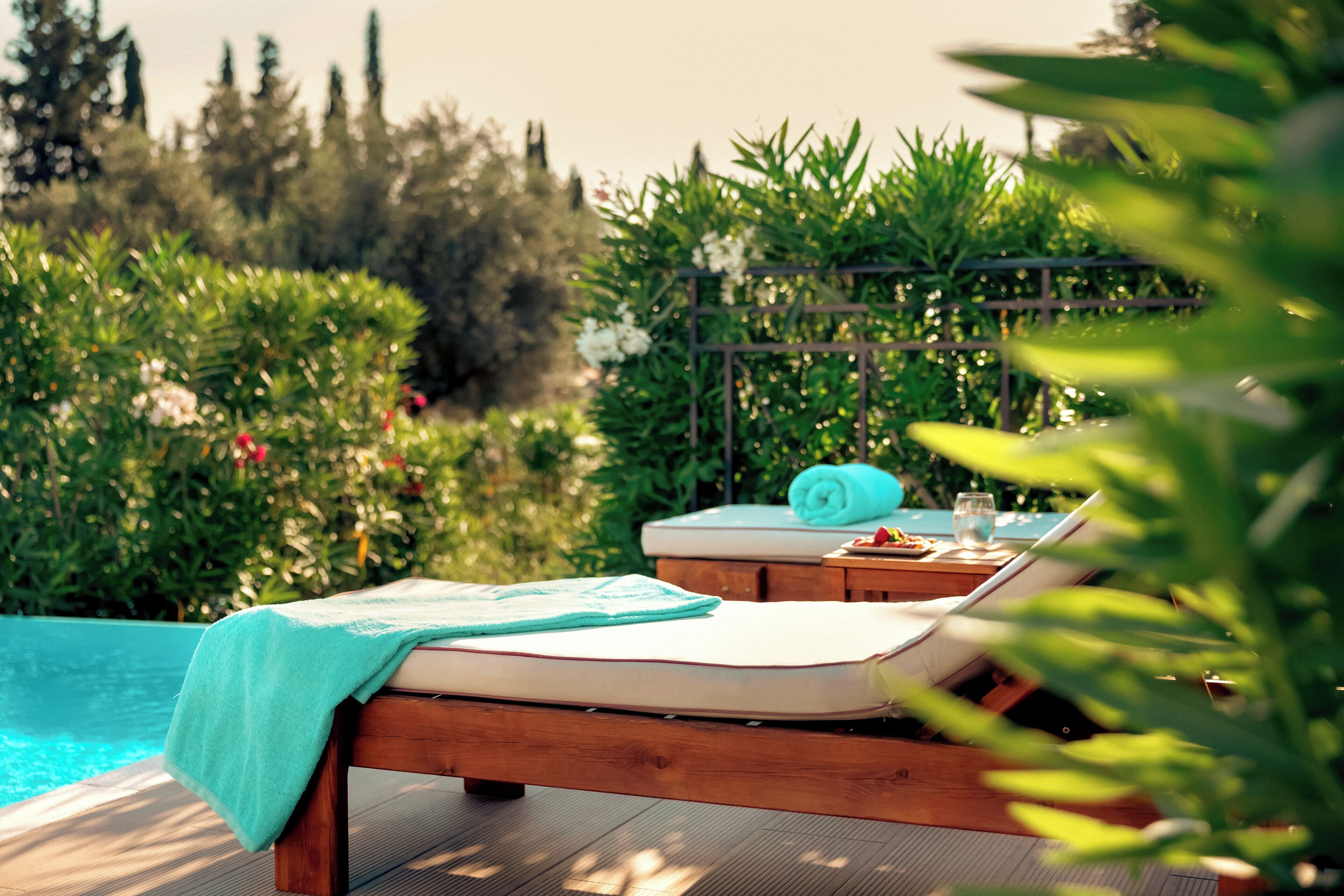 A wooden deck with two lounge chairs, a small table, and a pool in the background.
