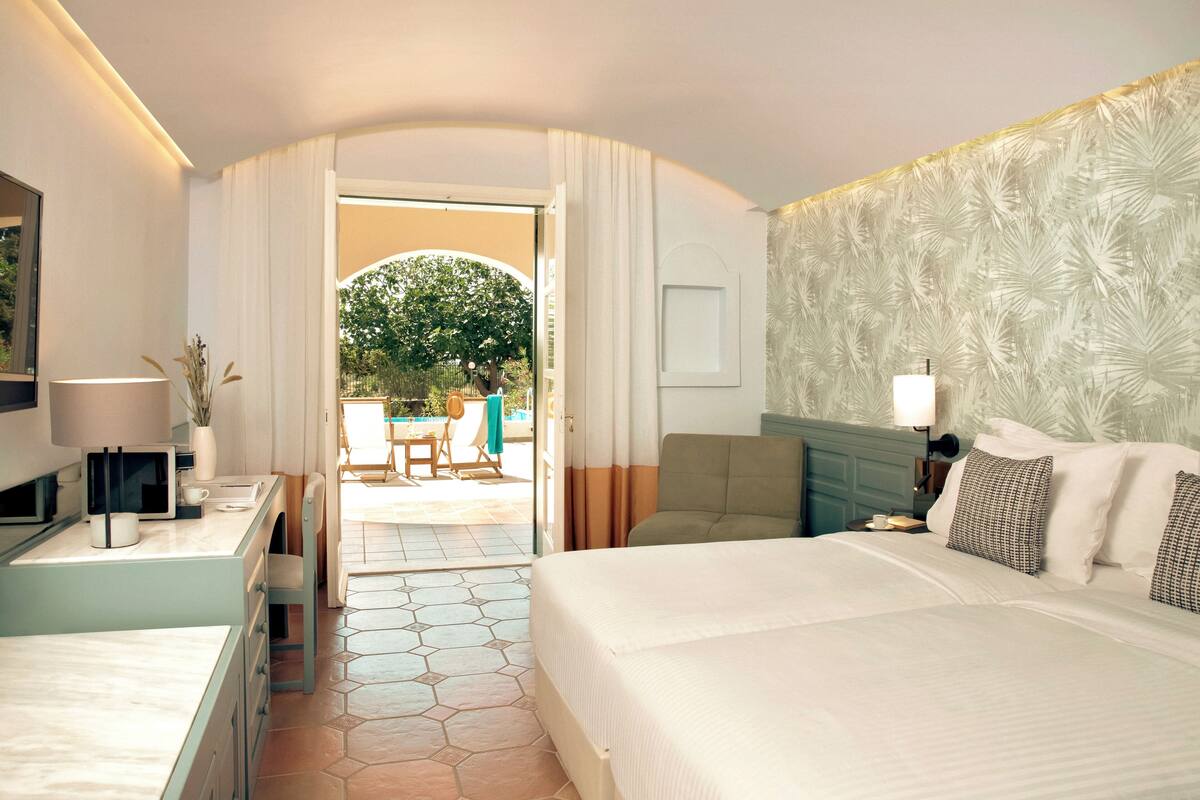 Een hotelkamer met een bed, een bureau, een stoel en uitzicht op een terras met een tafel en stoelen.