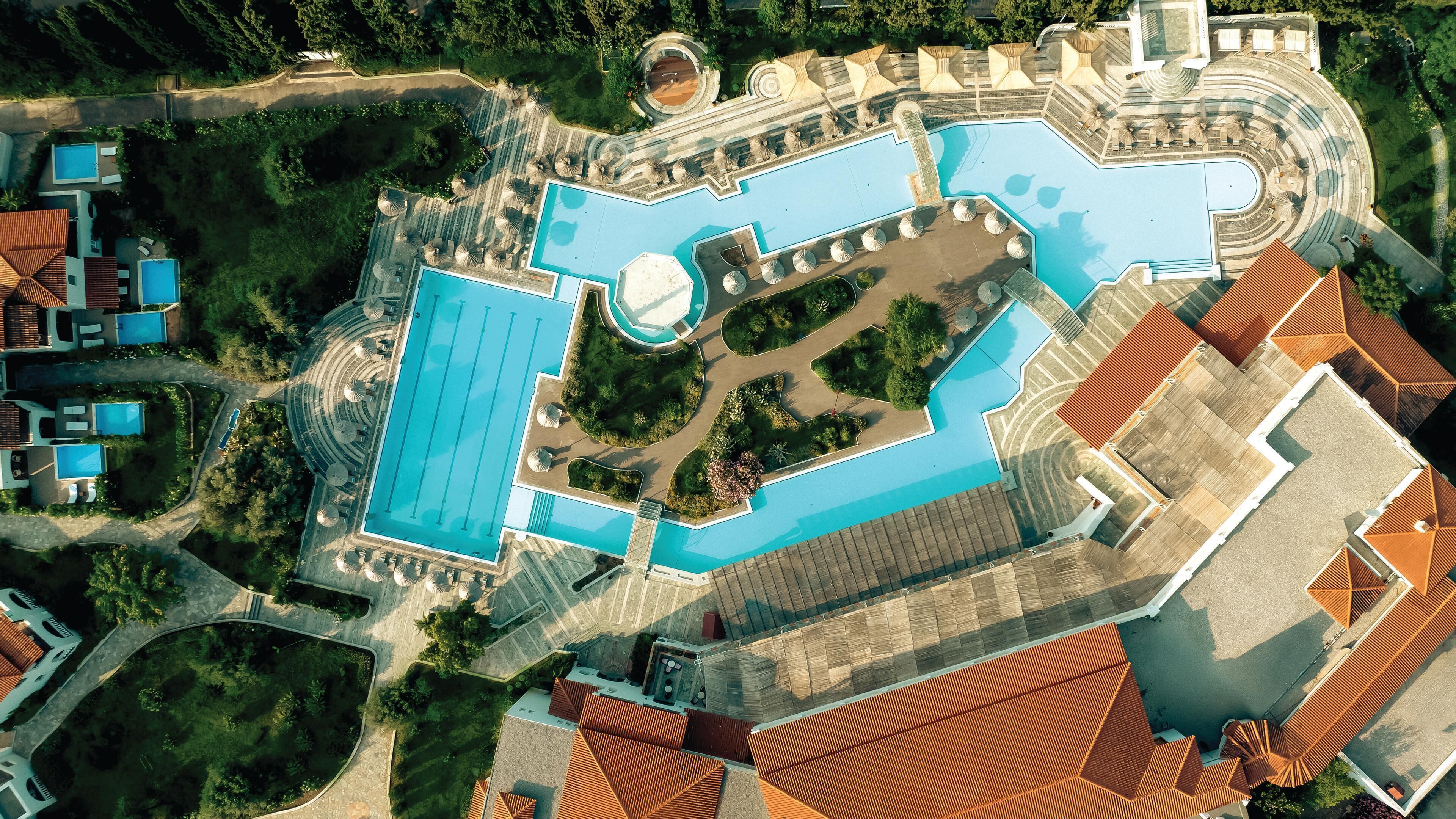 Vista aérea de un complejo turístico con varias piscinas, un patio central y villas circundantes.