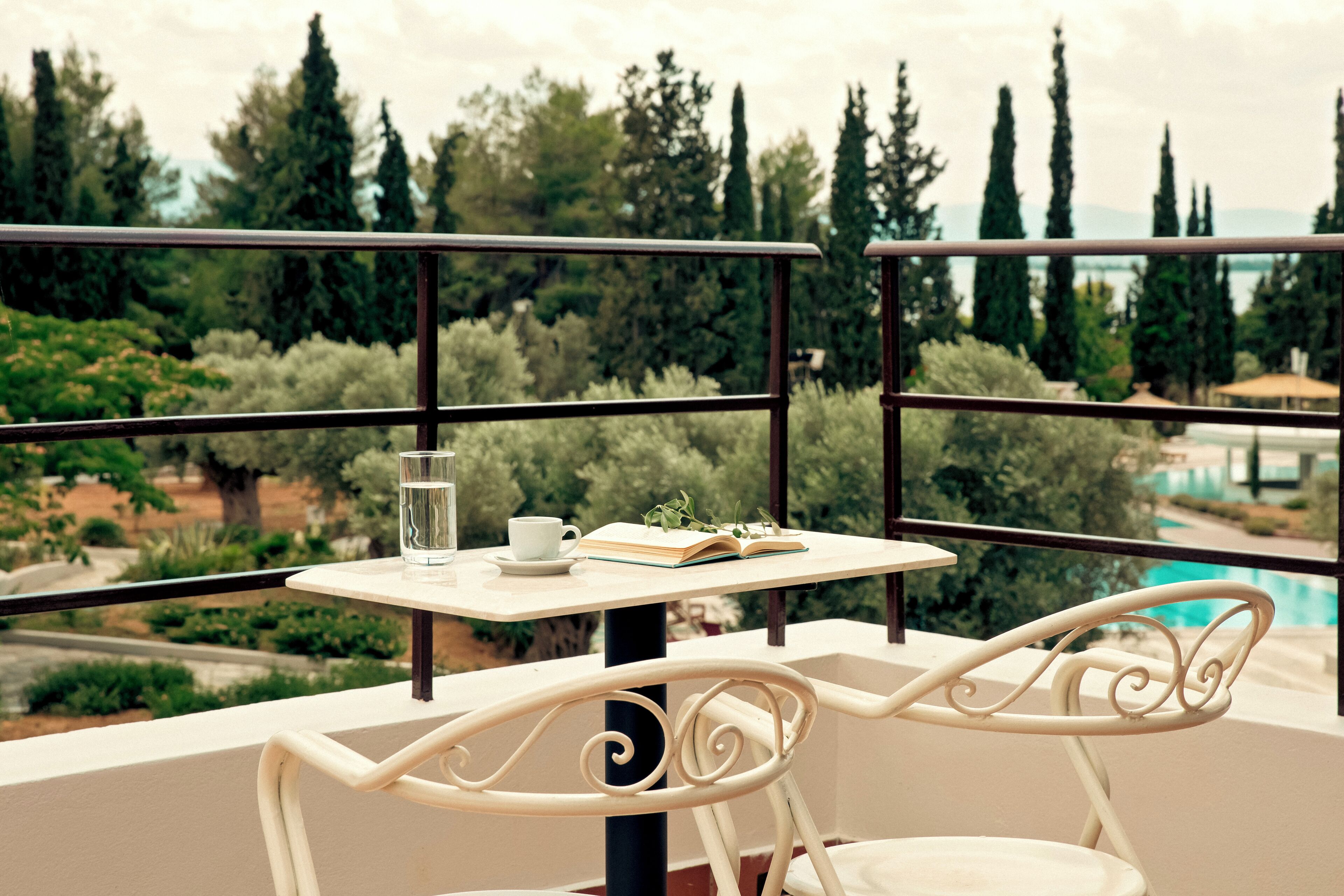 Un balcón con una mesa, una silla y vistas a una piscina y árboles.