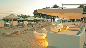 A beachside lounge area with sun loungers and umbrellas, a pool, and a covered seating area. - Zeus Eretria Resort  (Eretria)